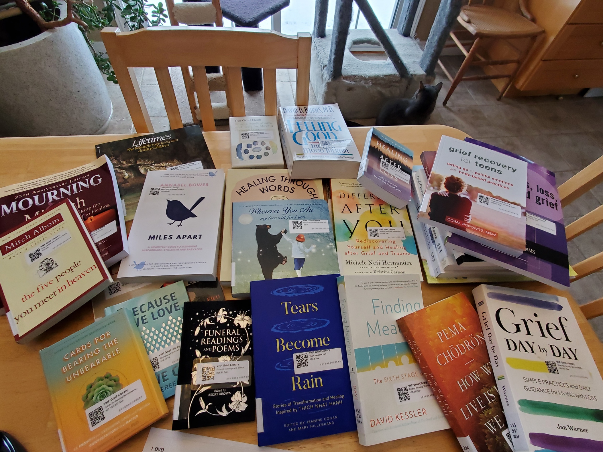 Piles of grief related books spread out on a wooden table. 