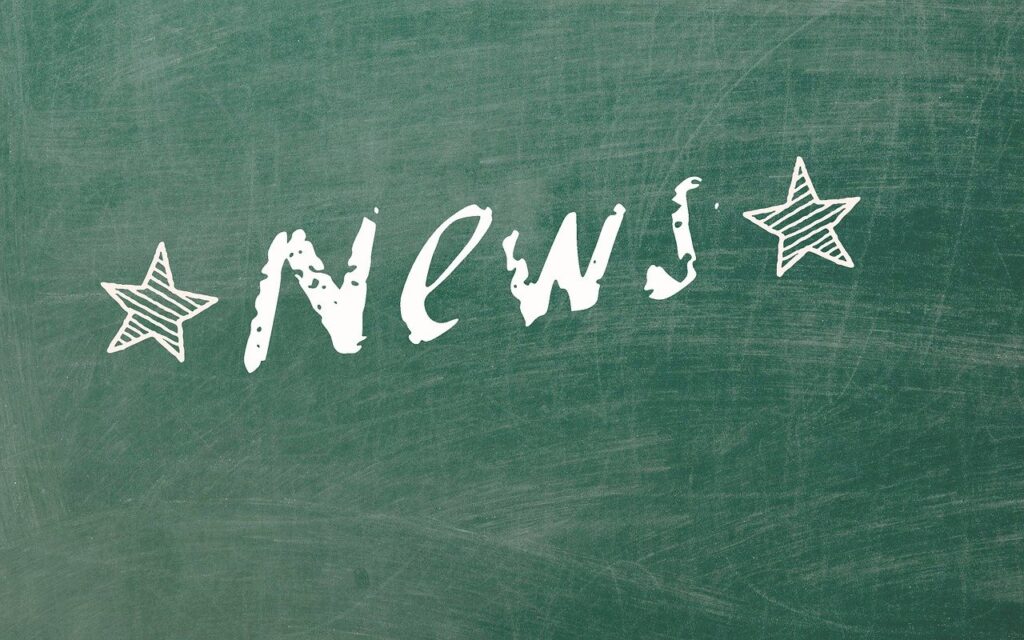 The word news written in white chalk on a dusty green blackboard. There are two white, striped, stars on either side of it.